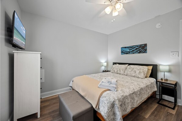 Ein Schlafzimmer mit Bett, Nachttischen, einem Fernseher, einem Deckenventilator und einem Bild an der Wand.