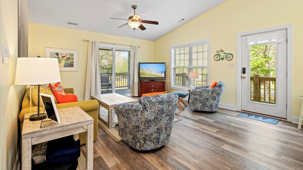Una sala de estar con ventilador de techo, televisor, mesa de comedor y dos sillones estampados.