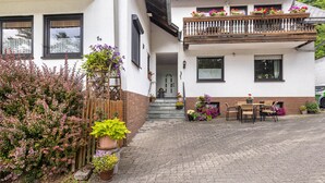 Un bâtiment à deux étages doté d’un balcon, d’une entrée pavée et d’un espace extérieur aménagé pour s’asseoir.