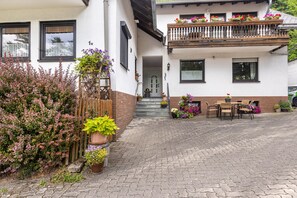 A two-story building with a balcony, a paved entrance, and outdoor seating. - Apartment 'Ferienwohnung am Golfplatz' Fewo A with Mountain View, Balcony and Wi-Fi (Willingen)