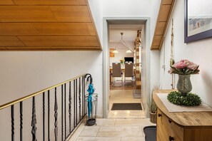 A hallway with a wooden staircase, a vase with flowers, and a dining area in the background. - Apartment 'Ferienwohnung am Golfplatz' Fewo A with Mountain View, Balcony and Wi-Fi (Willingen)