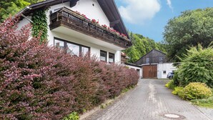 Un chalet traditionnel doté d’un toit à pente, d’un balcon en bois et d’un chemin menant à l’entrée.