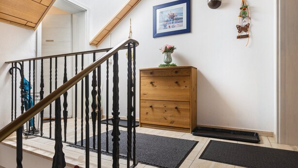 Un escalier avec une rampe en bois, une commode en bois, un tableau encadré et un objet décoratif fixé au mur.