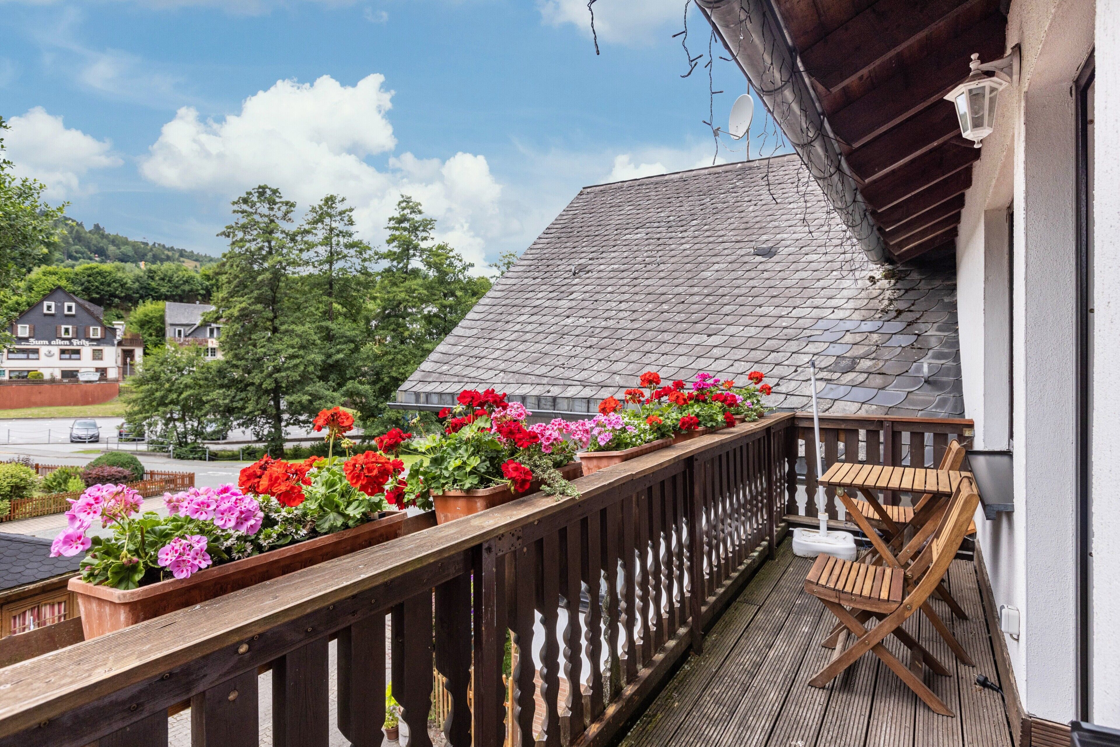 A balcony with wooden railings, potted flowers, and a wooden table and chair.