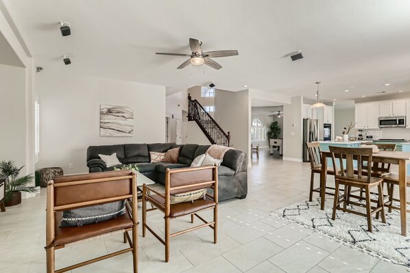 A spacious living area with a sofa, chairs, a dining table, and a kitchen in the background.