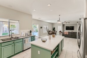 A modern kitchen with a central island, green cabinets, and a large refrigerator.