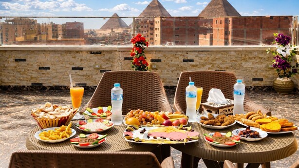 A rooftop dining table with a view of pyramids, featuring a variety of food and drinks. - Anubis pyramids view inn (Giza)