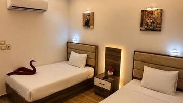 A hotel room with two beds, a nightstand, an air conditioner, and wall-mounted artwork.
