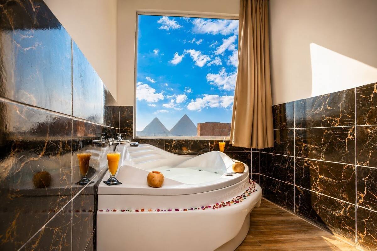 A luxurious bathroom with a large bathtub, a window with a view of pyramids, and marble walls.