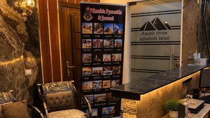 A reception area with a marble floor, a reception desk, a seating area with a sofa and chairs, and a wall with a poster featuring pyramids and a hotel name. - Anubis pyramids view inn (Giza)