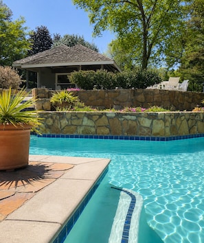 A swimming pool with a stone wall and potted plants.
