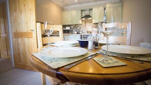 A dining area with a wooden table set for two, two wine glasses, and a blue bowl. - Friesian Cottage at The Dairy at Daviot (Inverness)