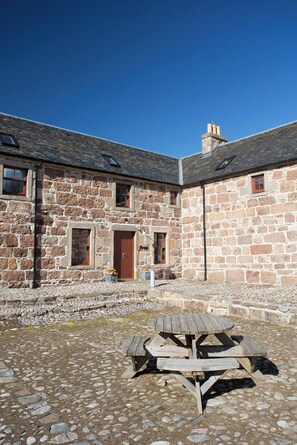 A stone building with a wooden door, windows, and a picnic table in front. - Friesian Cottage at The Dairy at Daviot (Inverness)