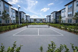 A tennis court surrounded by modern apartment buildings with a clear sky. - Modern King Bed Pool Gym Free Parking Near I95 (St. Augustine)