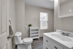 Un baño con inodoro, lavamanos y ventana con persianas.