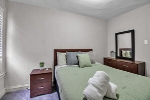Un dormitorio con cama, cómoda, mesita de noche, espejo y ventana con persianas.