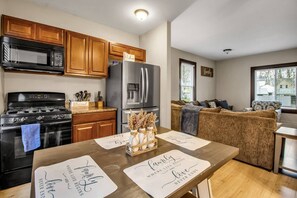 A modern kitchen with wooden cabinets, a black stove, a microwave, and a refrigerator. There is a dining table with placemats and a vase of dried flowers. - The Grand Gorge Getaway (Niagara Falls)
