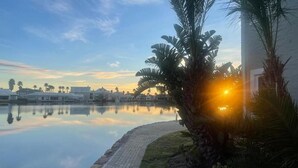 A serene lakeside view with a building, palm trees, and a clear sky. - Villa Martinique Canals (Jeffreys Bay)