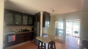 Uma cozinha com armários escuros, uma geladeira, um micro-ondas e uma pequena mesa com banquetas.