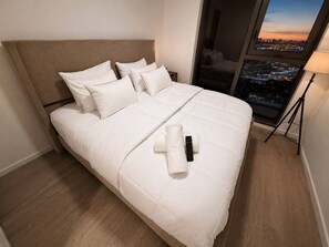 A hotel room with a bed, pillows, a remote control, and a lamp. - Luxury Downtown Condo | Skyline Views + Pool (Miami)