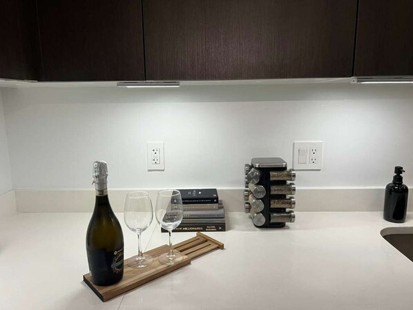 A kitchen counter with a wine bottle, two glasses, a wine rack, and a black bottle. - Luxury Downtown Condo | Skyline Views + Pool (Miami)