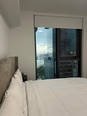 Un dormitorio con una cama grande, cabecera y vistas a un paisaje urbano a través de un ventanal.