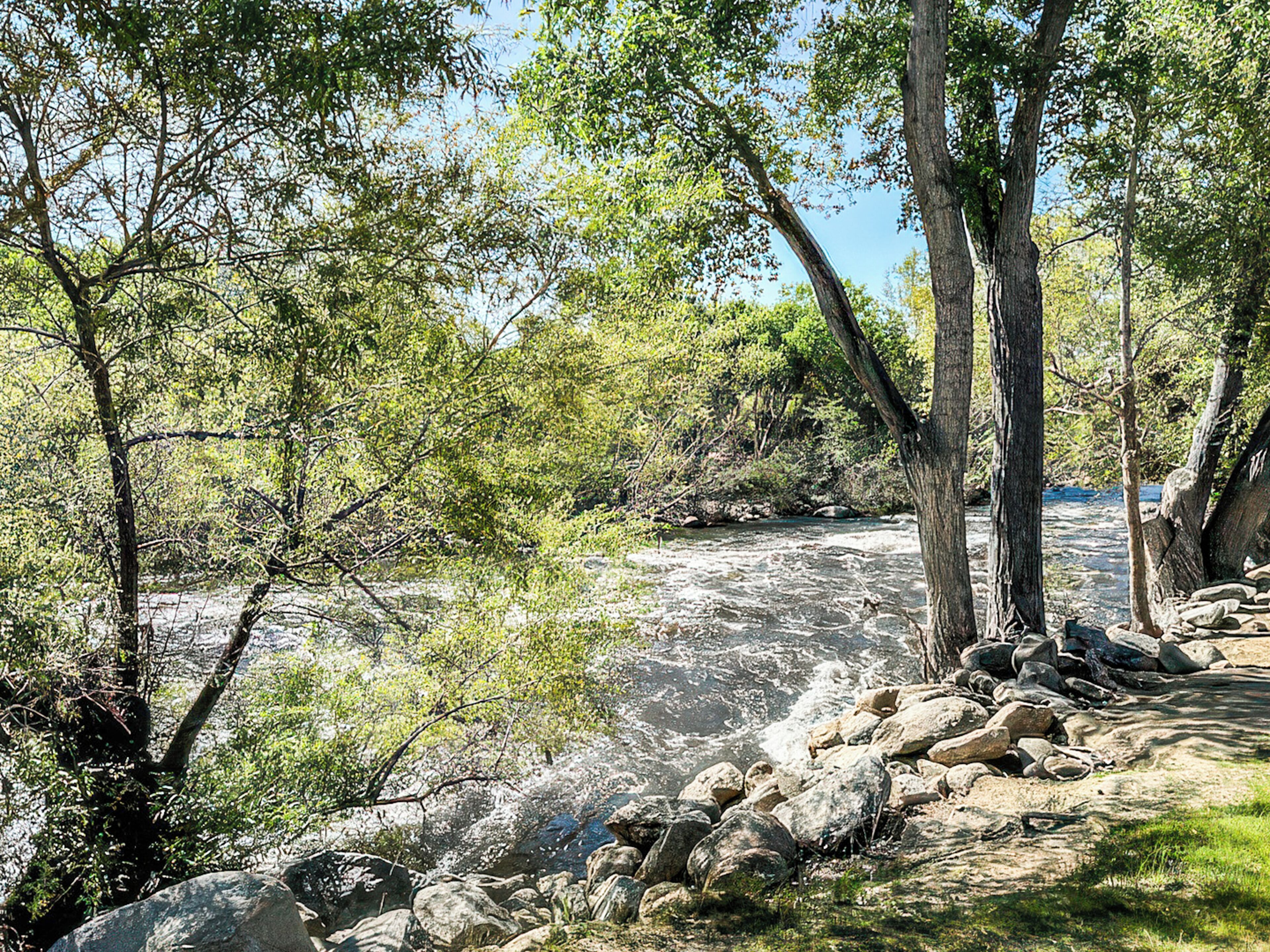 A natural landscape with a river, trees, and rocks.