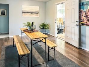 A dining area with a wooden table and benches, a painting on the wall, and a door leading to an outdoor space. - Stylish Getaway (Bodfish)