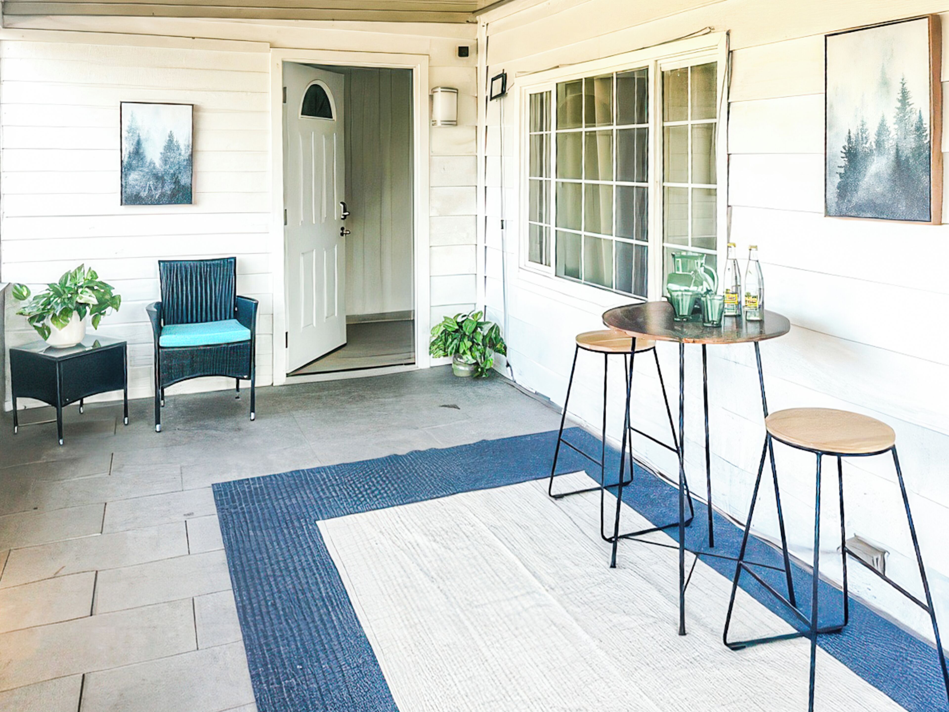 Una habitación con una puerta, dos sillas, una mesa con taburetes y dos plantas en macetas.