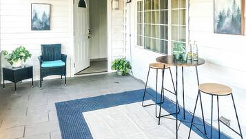 Una habitación con una puerta, dos sillas, una mesa con taburetes y dos plantas en macetas.
