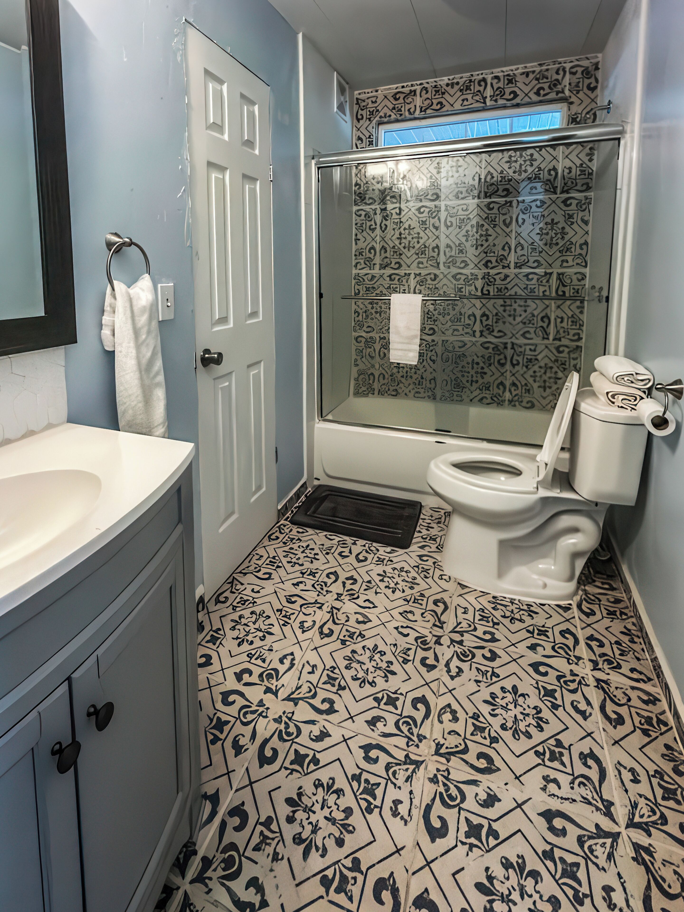 Un baño con un lavabo blanco, un inodoro, una ducha con puerta de cristal y baldosas de suelo estampadas.