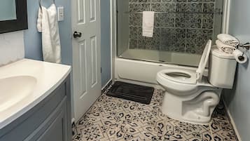 Un baño con un lavabo blanco, un inodoro, una ducha con puerta de cristal y baldosas de suelo estampadas.