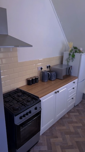 A compact kitchen with a gas stove, a toaster, a kettle, and a microwave on a wooden countertop. - Cozy 2-bedroom Apartment in Tyne and Wear (Gateshead)
