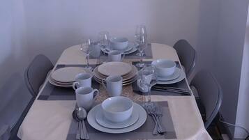 Una mesa de comedor dispuesta con platos, vasos, cubiertos, sillas, un cuadro en la pared y un mantel con motivos.