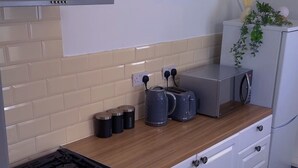 A compact kitchen with a gas stove, a toaster, a kettle, and a microwave on a wooden countertop. - Cozy 2-bedroom Apartment in Tyne and Wear (Gateshead)