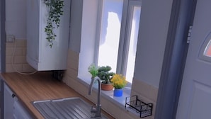A compact kitchen with a sink, a washing machine, a window with plants, and a door. - Cozy 2-bedroom Apartment in Tyne and Wear (Gateshead)