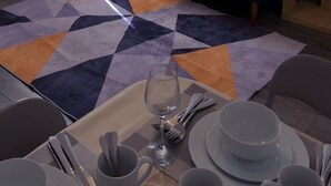 A living room with a blue sofa, a blue armchair, a patterned rug, a dining table set with plates, cups, and cutlery, and a lamp on a side table. - Cozy 2-bedroom Apartment in Tyne and Wear (Gateshead)