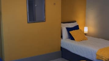 A hotel room with two beds, a window, a wall-mounted lamp, and a picture of a landmark.