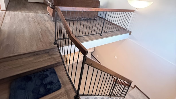Una escalera con barandilla de madera, un ventilador de techo, un televisor de pantalla plana y un cuadro en la pared.