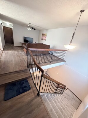 A staircase with a wooden railing, a ceiling fan, a flat-screen TV, and a painting on the wall.