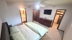 Un dormitorio con cama, cómoda, ventilador de techo, televisor y armario.