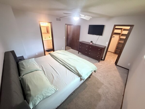 A bedroom with a bed, a dresser, a ceiling fan, a TV, and a closet.