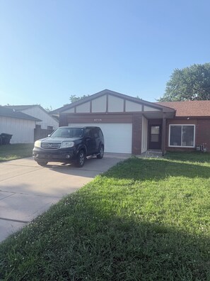 A residential garage with a black SUV parked in front, a clear sky, and a well-maintained lawn.