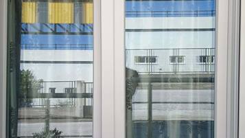 Une fenêtre donnant sur un immeuble à plusieurs étages et doté d’un balcon.