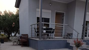 Un bâtiment doté d’un balcon, d’un escalier et d’un petit jardin avec un banc et une table.