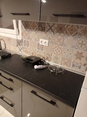 A kitchen with patterned tiles, a black countertop, and a microwave. - Jordan's Seaside Studio - 100m from the Beach - Nea Karvali (Nea Karvali)