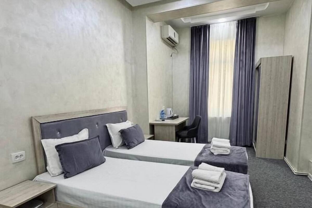 Quarto de hotel com duas camas, uma escrivaninha, uma cadeira e um guarda-roupa.