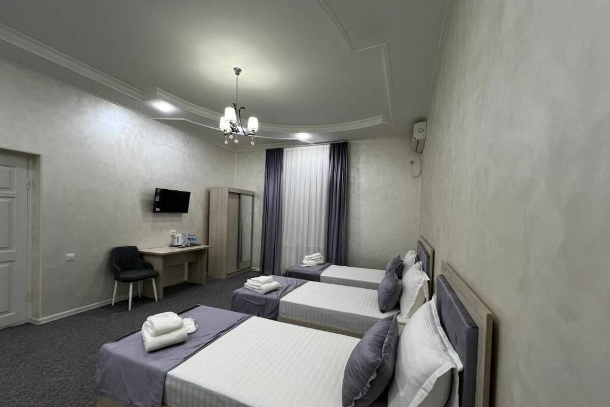 Quarto de hotel com duas camas, uma escrivaninha, uma cadeira, uma televisão e um candelabro.