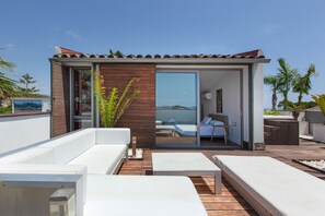 A modern outdoor lounge area with a wooden deck, white sofas, and a glass door leading to a pool area. - Villa 'Las Palmeras' for Families Only with Private Pool, Wi-Fi, and Air Conditioning (Canet de Mar)