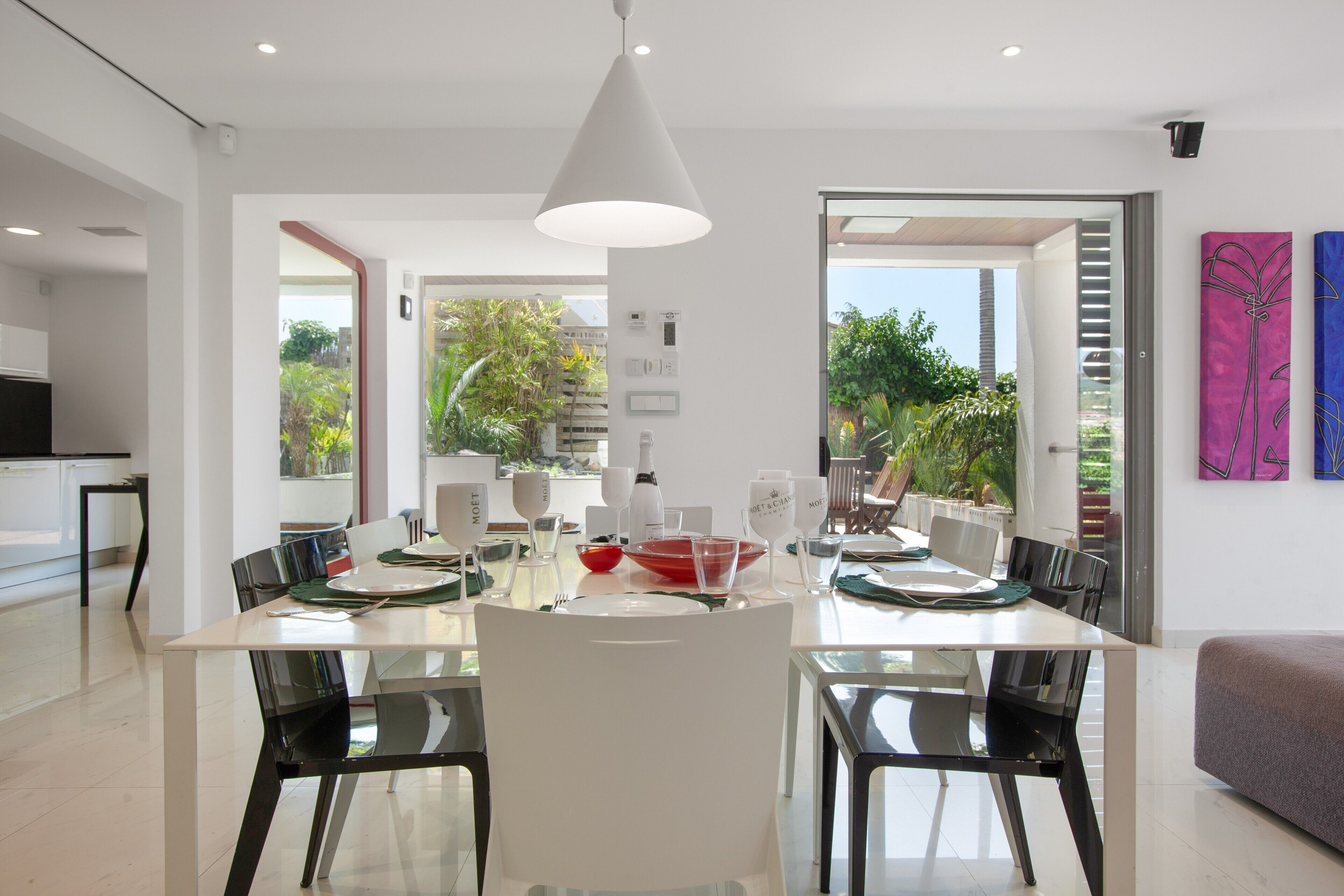 A modern dining area with a white table, black chairs, and a pendant light.